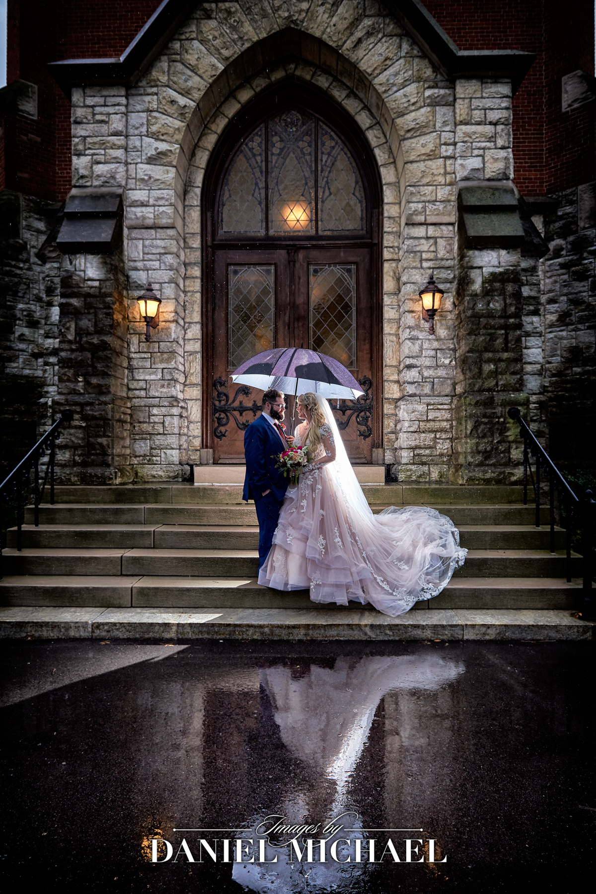 a rainy wedding photo with a bride and groom under an umbrella and their reflection in the water